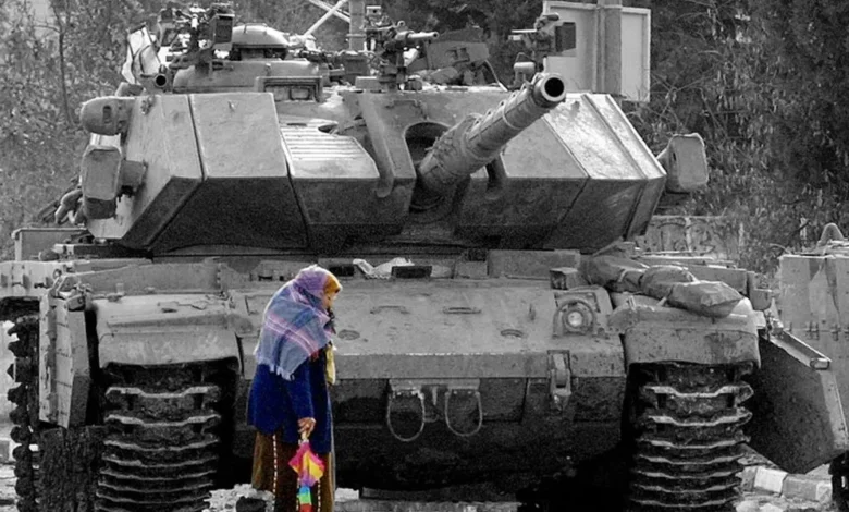 مسنة فلسطينية تمرّ أمام دبابة للاحتلال في طريقها إلى منزلها في بيتونيا بالضفة في كانون الأول 2001. عدسة ديفيد سيلفرمان