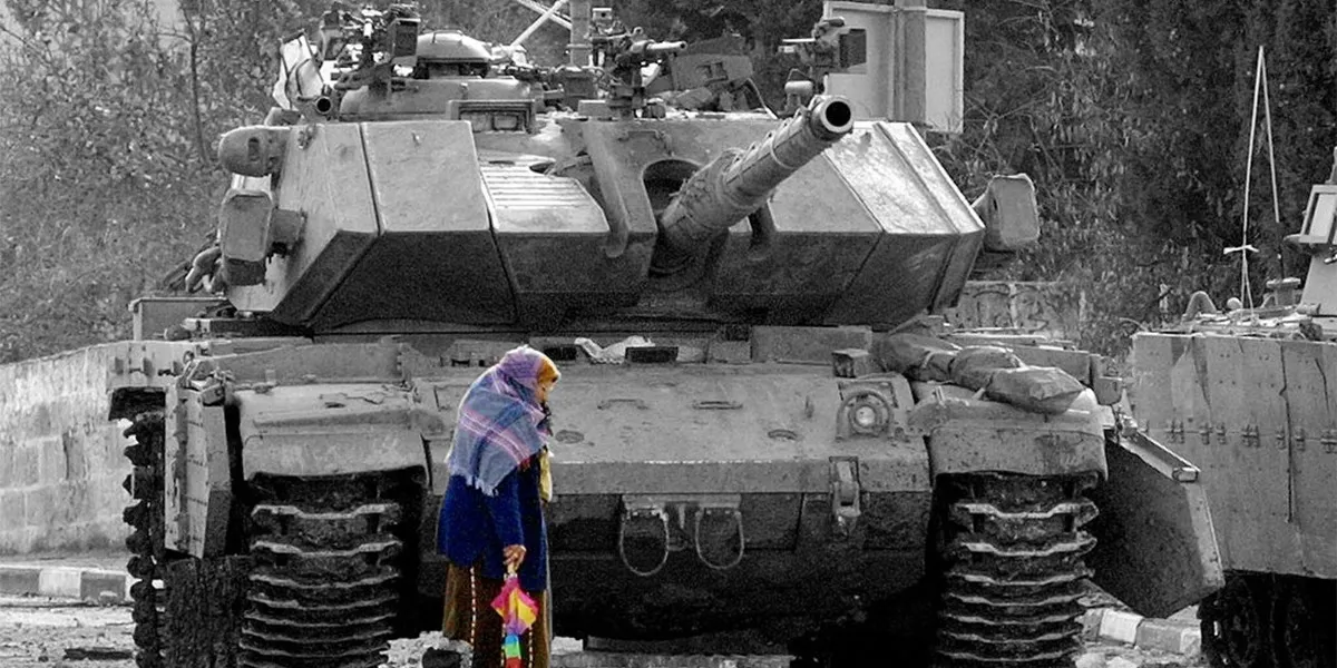 مسنة فلسطينية تمرّ أمام دبابة للاحتلال في طريقها إلى منزلها في بيتونيا بالضفة في كانون الأول 2001. عدسة ديفيد سيلفرمان